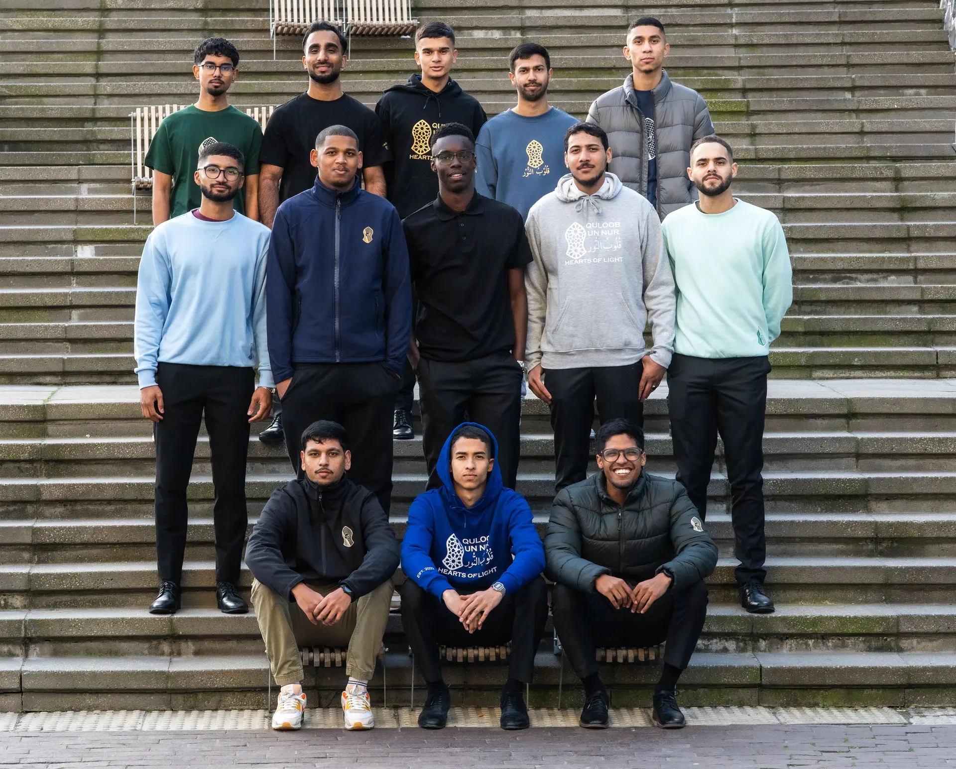 All 11 members of Quloob un Nur photographed together on the steps, wearing the new collection.