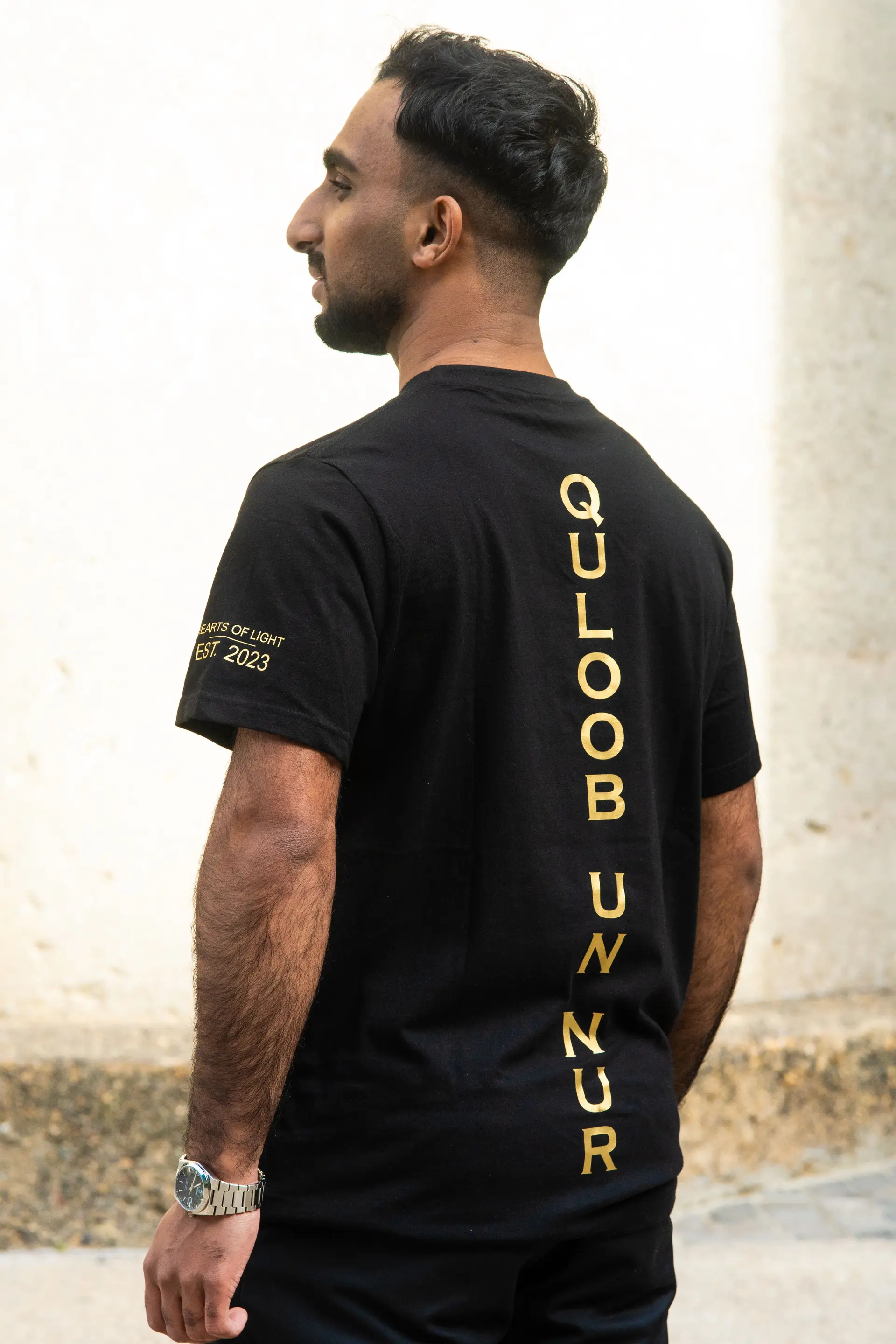 Black t-shirt from behind, gold name down the back
